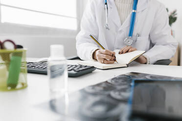 Arzt schreibt in Tagebuch sitzend am Schreibtisch im Krankenhaus - XLGF02745