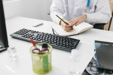 Arzt schreibt Notizen in Tagebuch sitzend in medizinischer Klinik - XLGF02757
