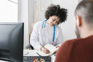 Doctor writing prescription for patient sitting at medical clinic - XLGF02768