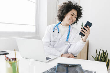 Glücklicher Arzt mit Laptop und Smartphone in der Klinik - XLGF02781