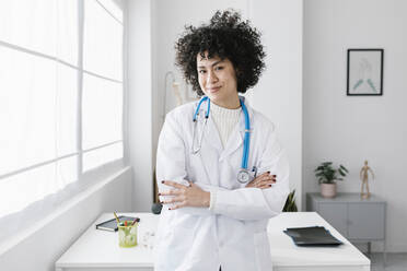 Smiling doctor standing with arms crossed at medical clinic - XLGF02788