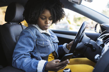 Junge Frau, die im Auto sitzend ein Mobiltelefon benutzt - JCCMF05470