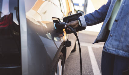 Young woman charging electric car at station - JCCMF05489