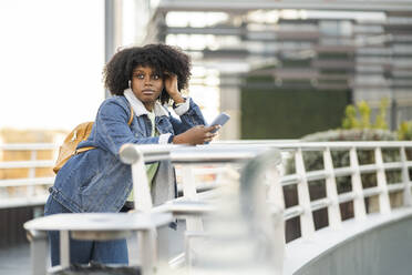 Junge Frau mit Smartphone, die sich an ein Geländer lehnt - JCCMF05496