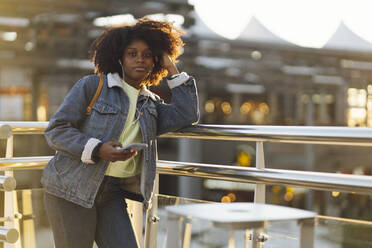 Woman with smart phone leaning on railing at sunset - JCCMF05498