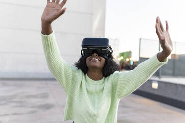 Happy young woman wearing virtual reality simulator at sunset - JCCMF05501
