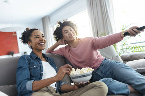 Happy women watching TV sitting on sofa in living room at home - JSRF01886