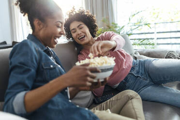 Fröhliche Freunde, die zu Hause auf dem Sofa sitzend Popcorn genießen - JSRF01888