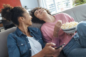 Cheerful friends talking with each other sitting on sofa at home - JSRF01889