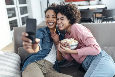 Glückliche Freunde nehmen Selfie durch Handy sitzen auf Sofa im Wohnzimmer - JSRF01891