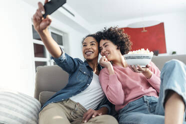 Frau nimmt Selfie mit Freund essen Popcorn sitzen auf Sofa zu Hause - JSRF01892