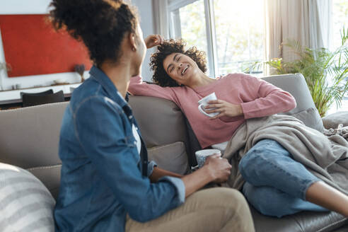 Glückliche Freunde mit Kaffeetasse auf dem Sofa sitzend zu Hause - JSRF01894