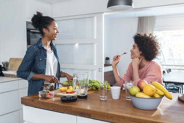 Young woman talking with friend cutting fruit in kitchen - JSRF01903