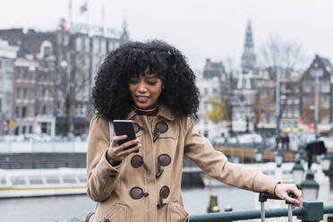 Young woman with curly hair using smart phone in city - PNAF03351