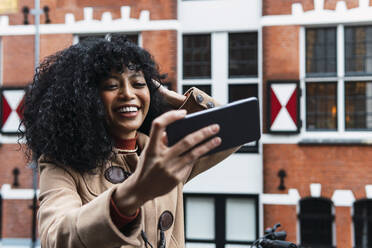 Glückliche junge Frau mit Hand im Haar, die ein Selfie mit ihrem Handy macht - PNAF03366