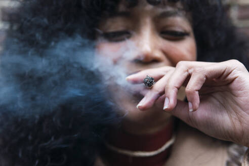 Lächelnde junge Frau beim Rauchen einer Zigarette - PNAF03378