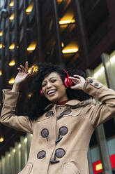 Cheerful young woman with eyes closed enjoying music through wireless headphones in city - PNAF03390