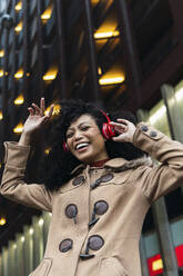 Fröhliche junge Frau mit geschlossenen Augen, die in der Stadt Musik über drahtlose Kopfhörer hört - PNAF03390