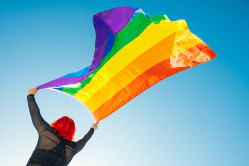 Woman on her back with open arms waving an lgbt flag - CAVF95394