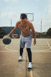 Young tattooed Latino boy playing with a basketball on a court - CAVF95399