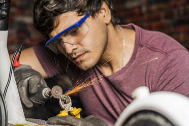 Ein Mechaniker mit Schutzbrille benutzt einen Mini-Schleifer, um eine Schraube zu schneiden - CAVF95410