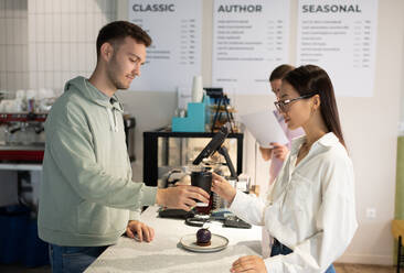 Mann serviert einer Frau im Café eine Bestellung - CAVF95441