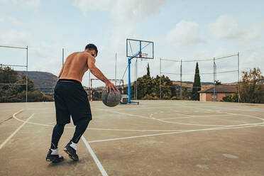 Junge trainiert allein auf einem Basketballplatz - CAVF95464