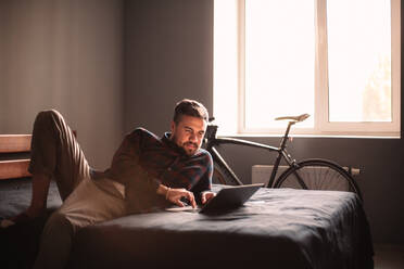 Happy man using laptop computer on bed at home - CAVF95517