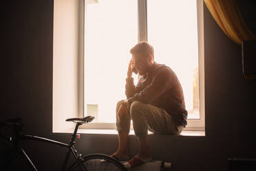 Mann spricht mit seinem Smartphone auf der Fensterbank zu Hause - CAVF95519