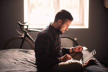 Happy man using credit card and laptop computer shopping online - CAVF95521