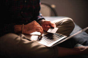 Man using credit card and laptop computer shopping online at home - CAVF95523