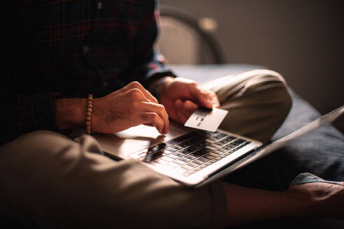 Mann mit Kreditkarte und Laptop beim Online-Einkauf zu Hause - CAVF95523