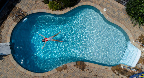 Overhead view of woman floating in a swimming pool on summer day. - CAVF95529