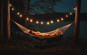 Ein Paar liegt an einem Sommerabend am See in einer Hängematte. - CAVF95535