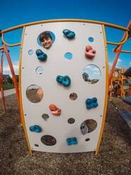 Happy boy peeking through holes in climber at a playground. - CAVF95537