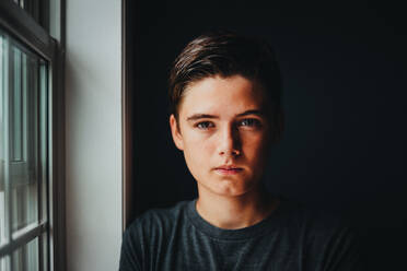 Close up portrait of serious teenage boy in a dark room. - CAVF95544