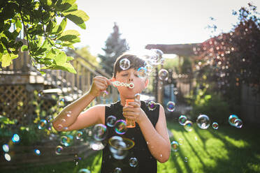 Young boy blowing bubbles in a backyard on a sunny day. - CAVF95545