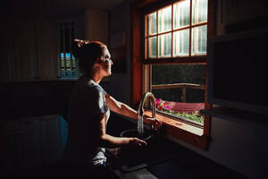 Frau füllt einen Topf an der Spüle unter einem Fenster in einer dunklen Küche. - CAVF95553