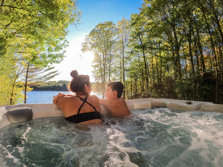 Boy and his mom relaxing in a cottage hot tub with a lake view. - CAVF95554