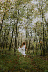 Woman in white dress running through a clearing in the woods. - CAVF95556