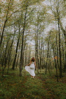 Frau in weißem Kleid läuft durch eine Waldlichtung. - CAVF95556
