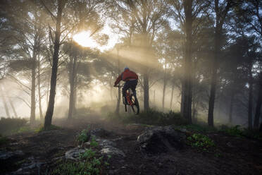 Ein junger Mountainbiker springt an einem wunderschönen nebligen Morgen. Spanien - CAVF95573