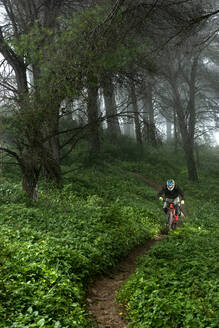 Junger Mountainbiker fährt schnell an einem schönen nebligen Morgen in Spanien - CAVF95574