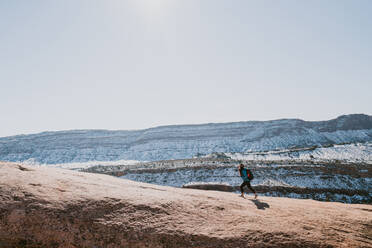 A woman wearing brimmed hat and backpack hikes alone in desert - CAVF95589