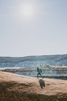 Eine Frau mit Hut mit Krempe und Rucksack wandert in der Wüstenlandschaft - CAVF95590
