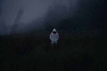 Ein mysteriöser Mann mit weißem Kapuzenpulli in einem dunklen, nebligen Wald - CAVF95595