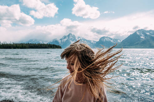 Junges Mädchen wirft ihr Haar an einem sonnigen Tag in der Nähe eines Sees nach draußen - CAVF95648
