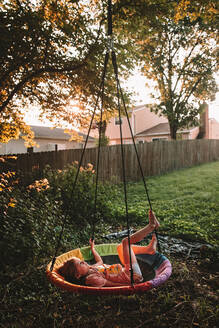 Swinging on her tree swing at sunset - CAVF95675