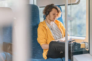 Junger Mann, Teenager, reist mit Kopfhörern im Zug - CAVF95676