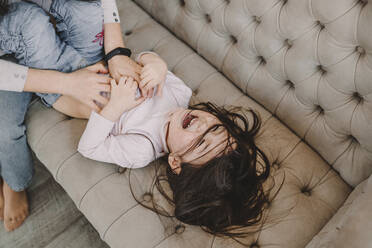 Mother tickling daughter on sofa at home - ORF00012